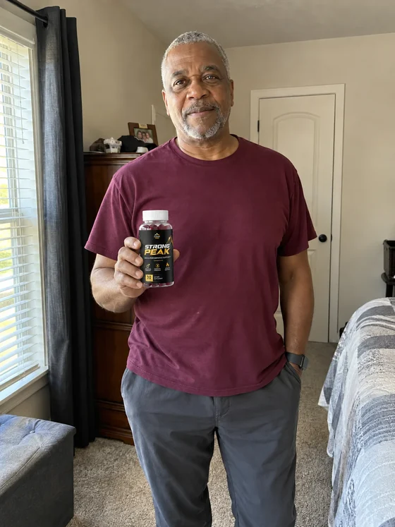 Confident man holding a Strong Peak gummy bottle in his home